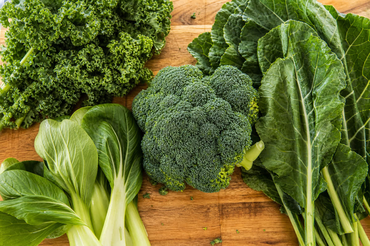 Fresh leafy green vegetables including kale broccoli and bok choy on a wooden cutting board