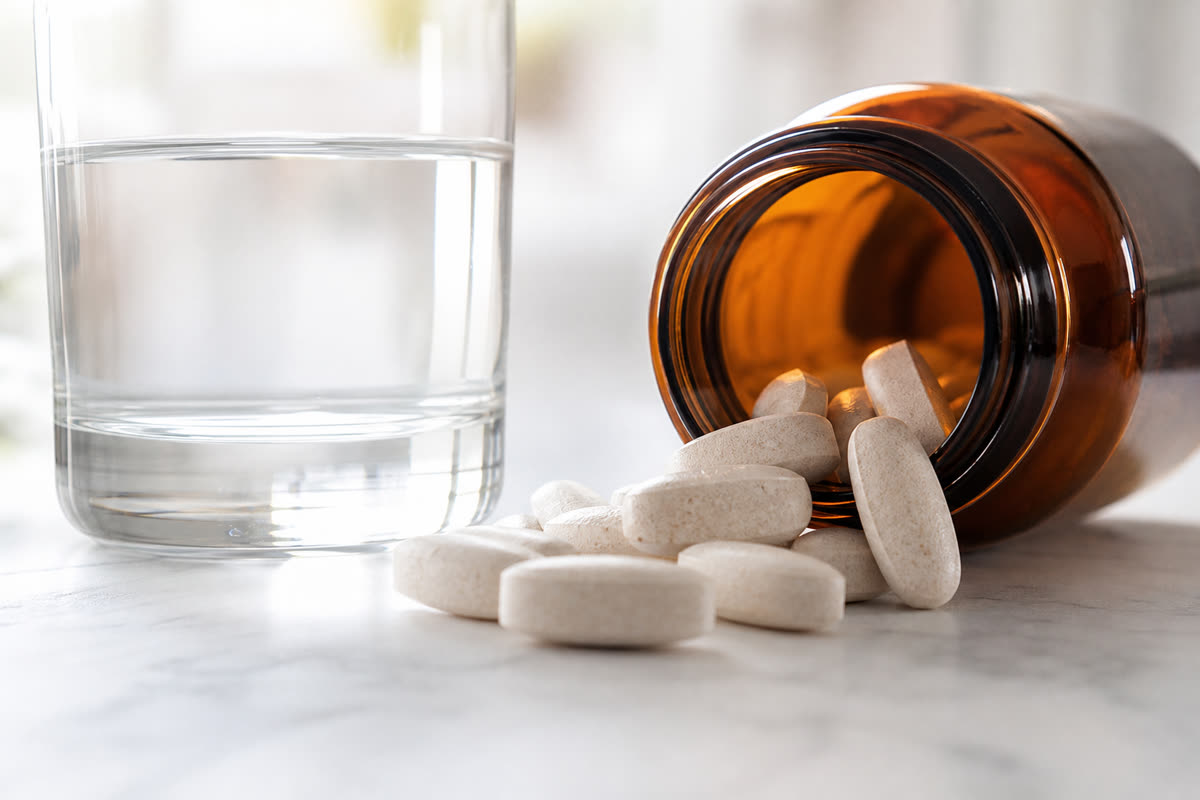 Calcium supplement tablets spilling from an amber bottle next to a glass of water