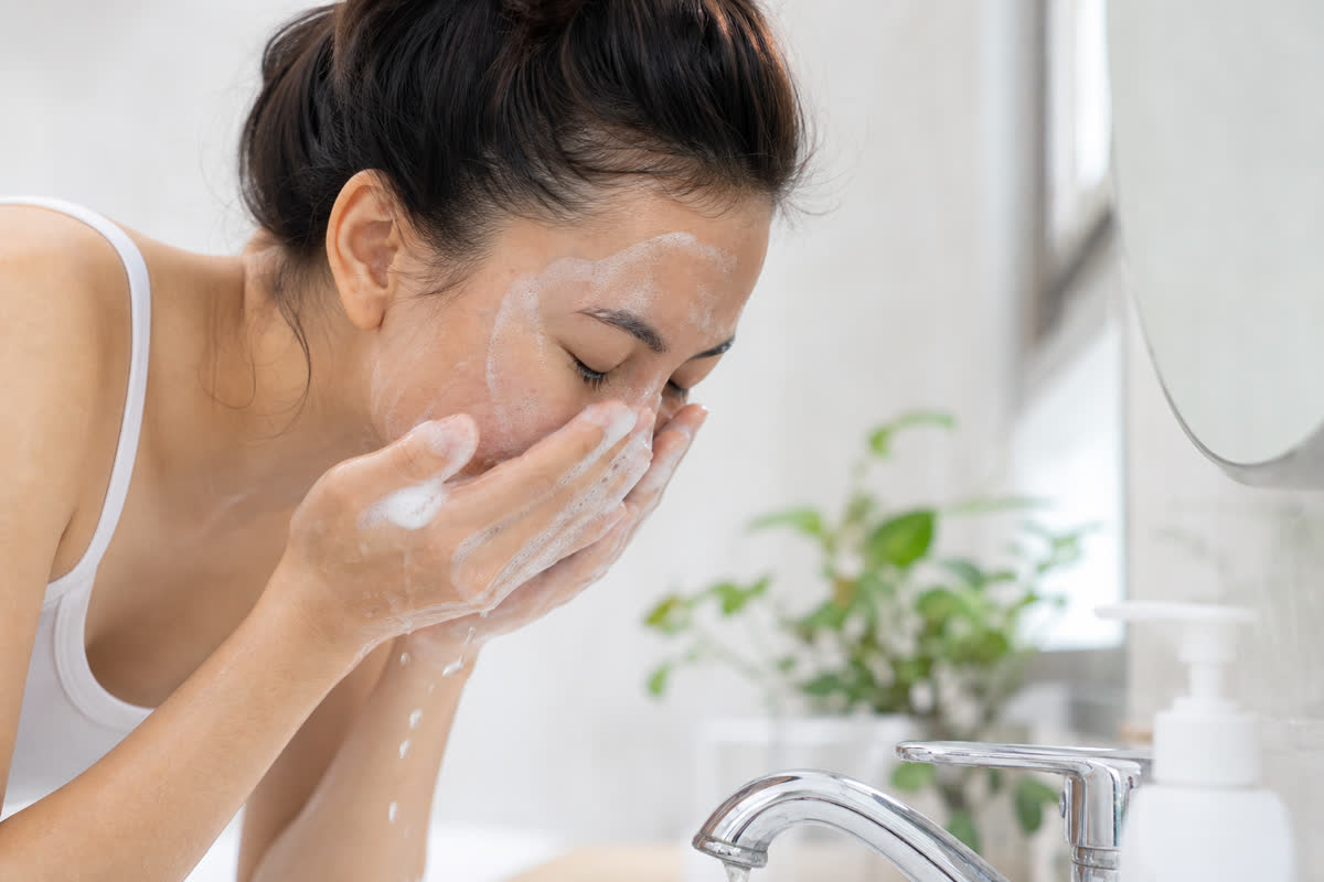 Young woman gently washing her face with a foaming cleanser at a bright bathroom sink