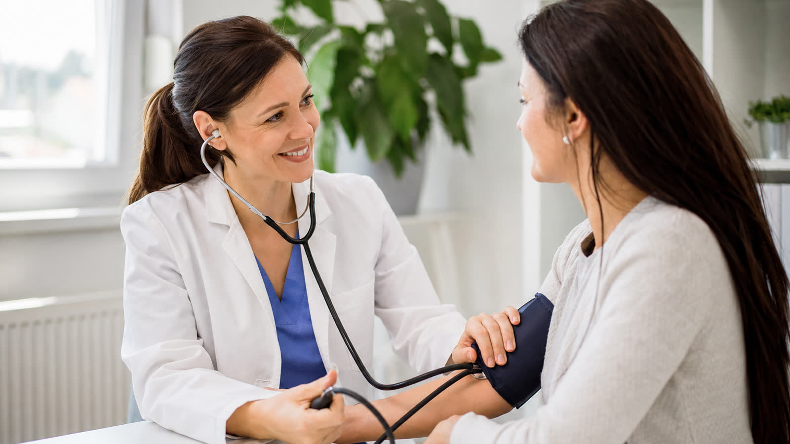 Doctor measuring a patient's blood pressure with a cuff in a bright modern clinic while discussing symptoms