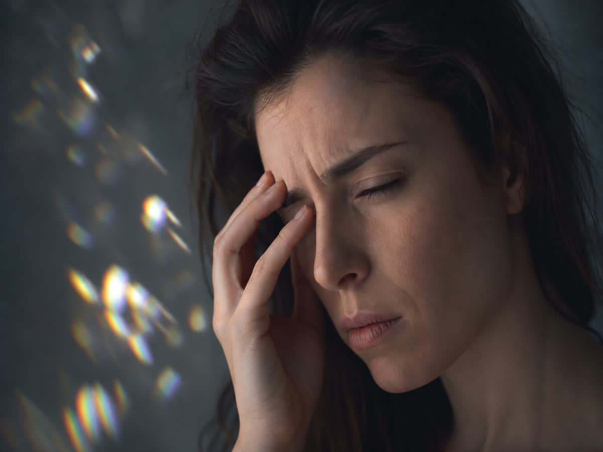 Close-up of a woman shielding her eye with soft shimmering light spots suggesting a migraine visual aura