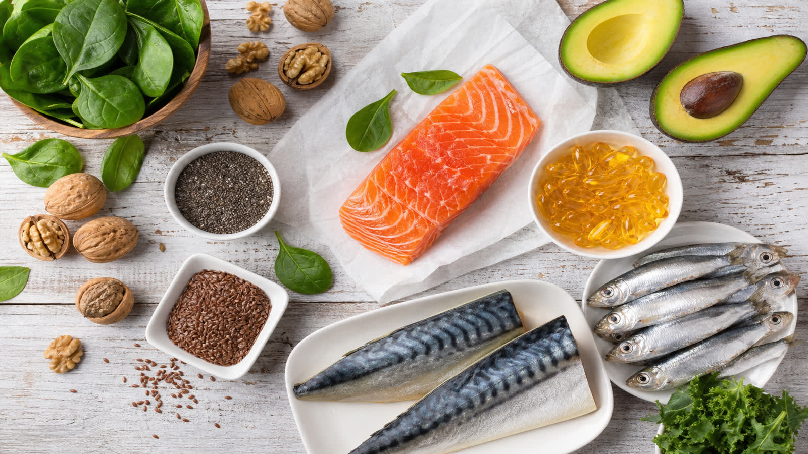 Flat lay of omega-3 rich foods including salmon sardines walnuts chia seeds flaxseeds avocado and fish oil capsules on a wooden table