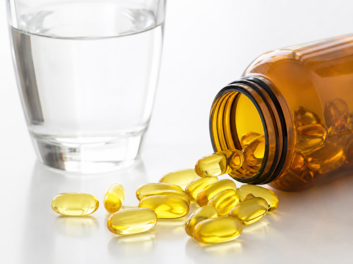 Golden omega-3 fish oil softgel capsules spilling from an amber bottle next to a glass of water
