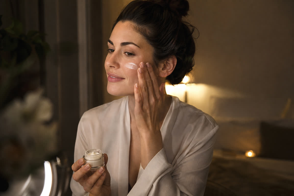 Woman applying retinol night cream to her face in softly lit room during her evening skincare routine