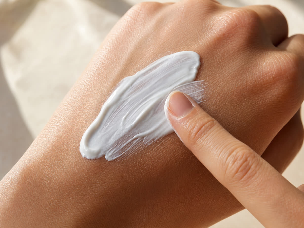 A generous dollop of white sunscreen cream being spread across the back of a hand showing proper application amount