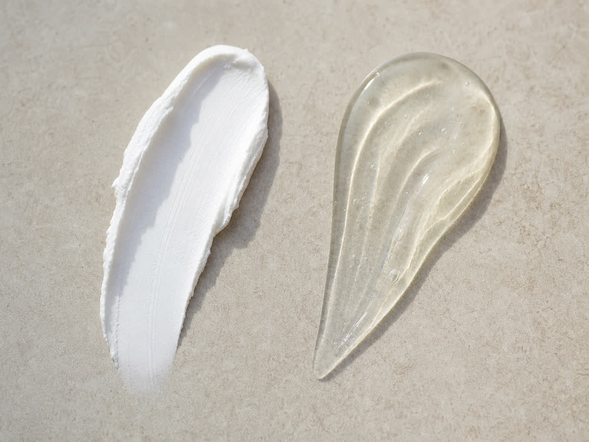 White mineral zinc sunscreen cream beside a clear chemical sunscreen lotion on a neutral stone surface